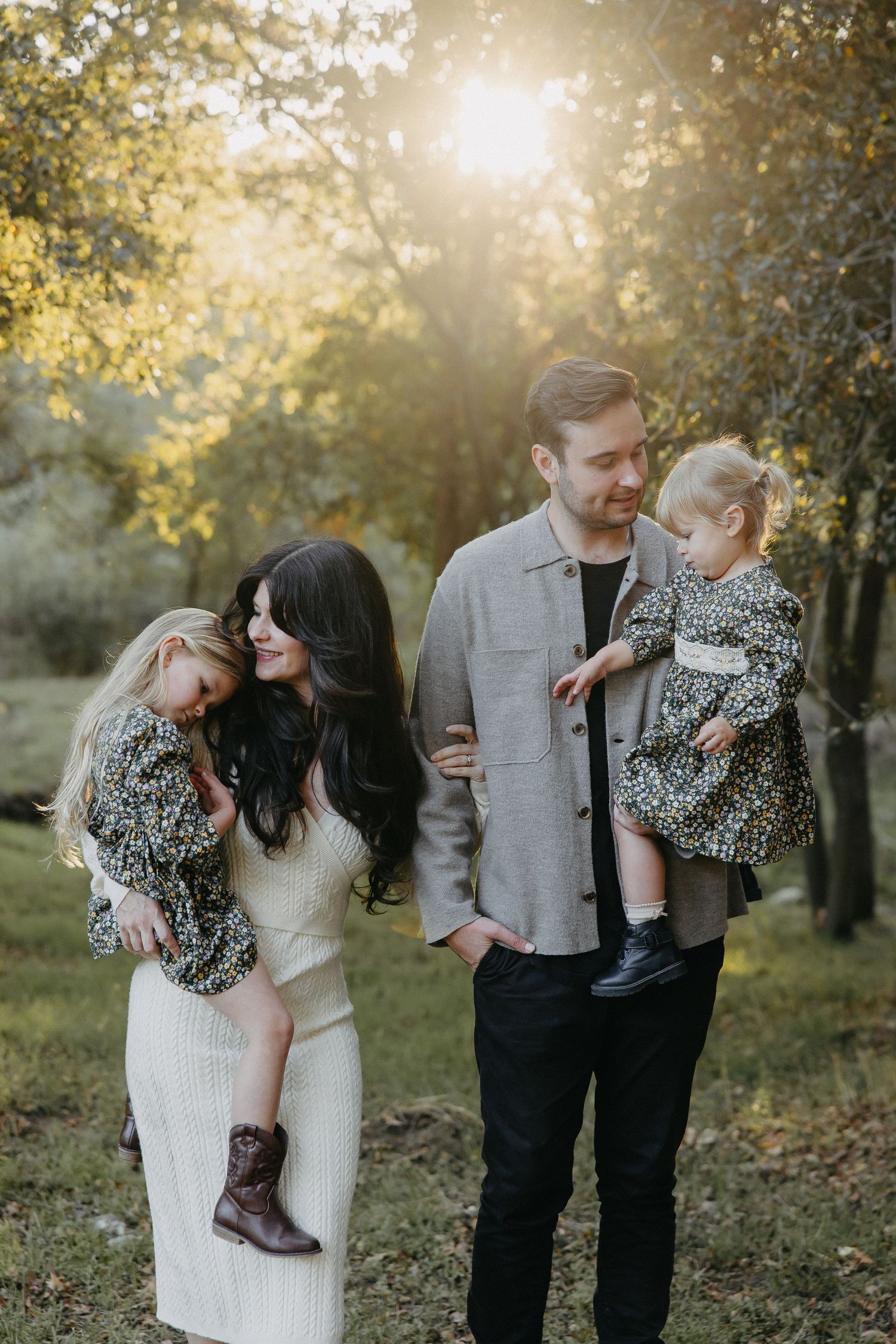 Family shares tender moments while posing in a sunlit garden with fall foliage in the background.