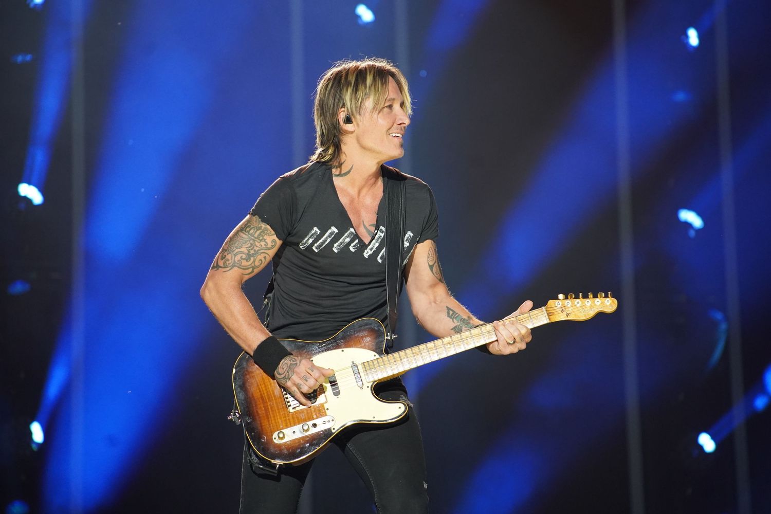 A musician plays electric guitar under dramatic blue stage lighting during a concert performance.