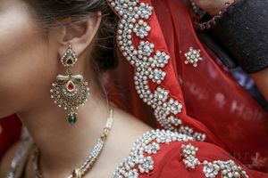 Close-up of a bride wearing ornate gold chandelier earrings and pearl-embroidered red bridal lehenga dupatta.