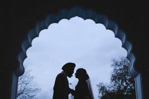 Silhouette of a Sikh couple sharing an intimate moment framed by an ornate arch at their wedding.