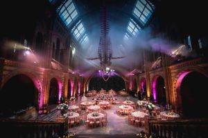 Elegant wedding reception in a grand hall with pink uplighting and a whale skeleton overhead.
