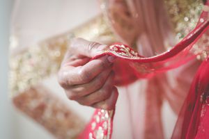Close-up of hands adjusting a red and gold embroidered bridal dupatta during an Indian wedding ceremony.