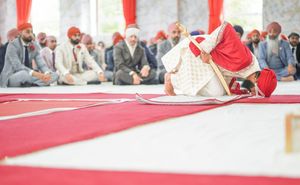 Sikh groom bowing in prayer during traditional Anand Karaj wedding ceremony with guests seated on red carpet.