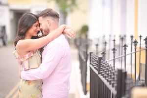 Romantic couple embracing and smiling outdoors near decorative iron railings on a charming urban street.