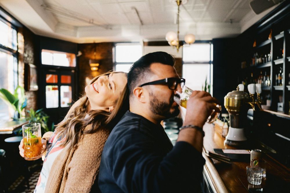 Couple enjoying drinks at a stylish bar, woman laughing while man sips cocktail, cozy ambiance.