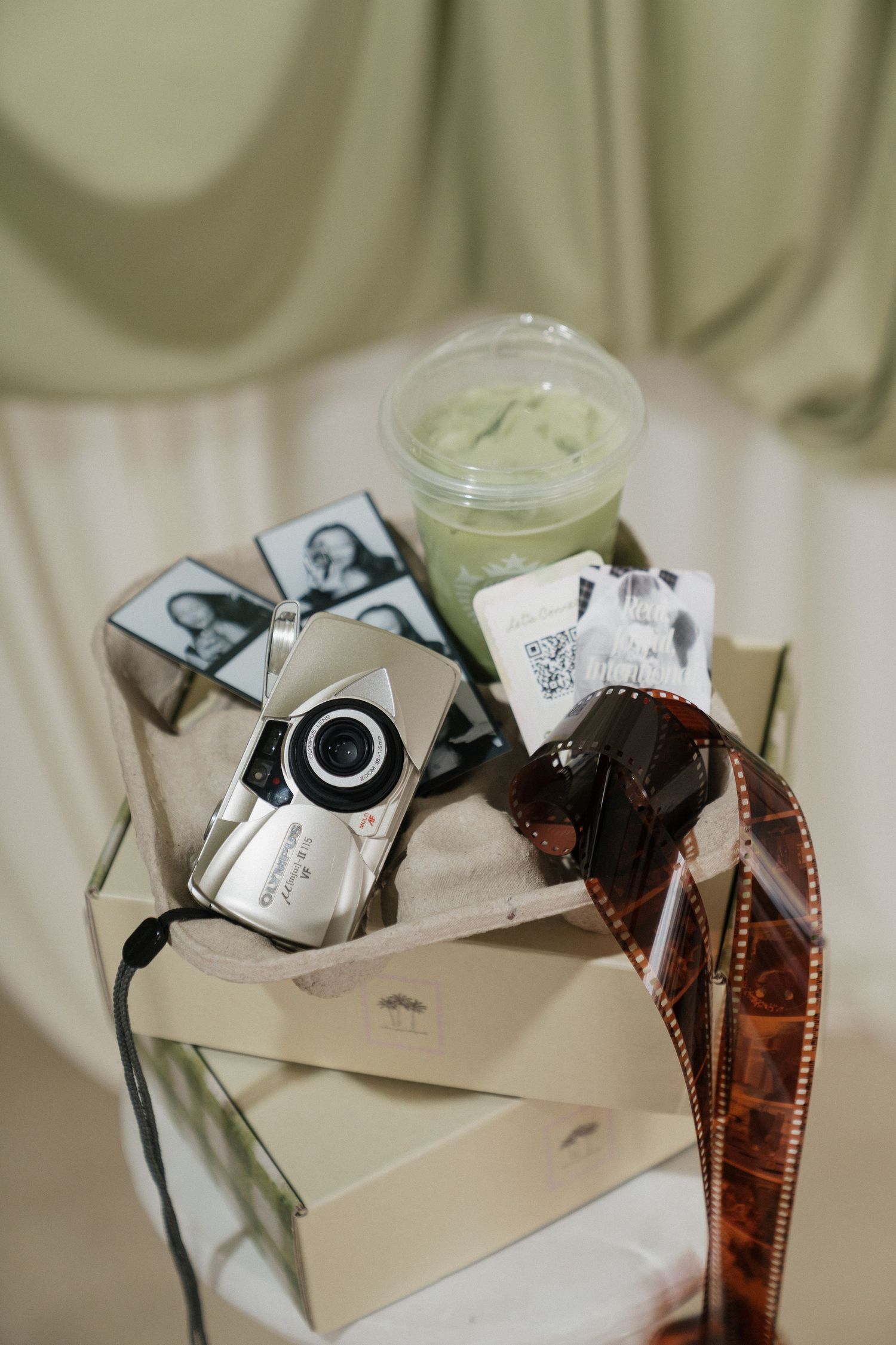 Vintage film camera, photo strips, film negatives, and a green matcha drink arranged in a decorative gift box display.