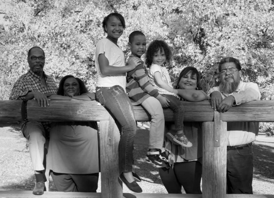 Two sets of grandparents and three grandchildren pose for a photo at a park.