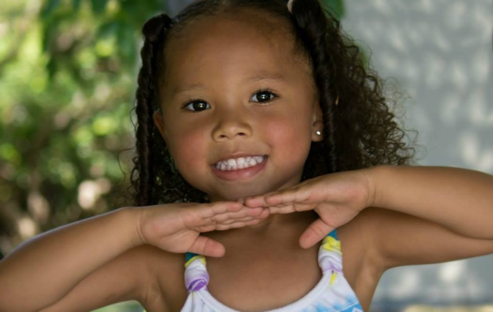 A young girl poses with her hands under her chin.