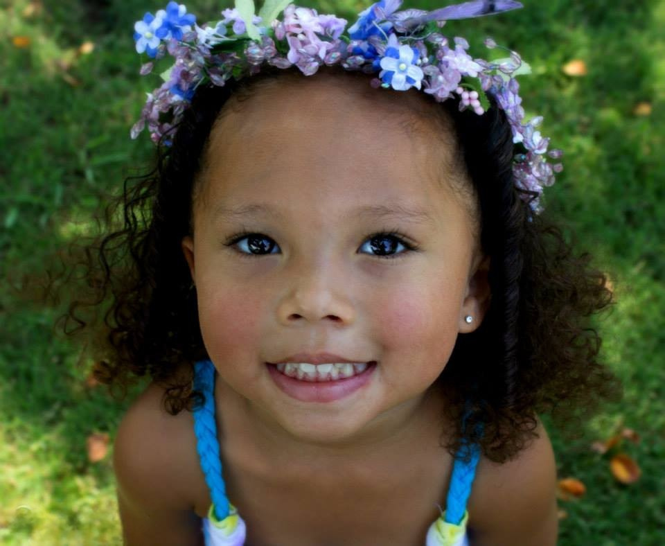A young girl wearing a flower crown looks up at the camera lens while posing for a photo.