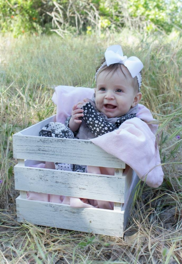 An infant girl poses for a photo while sitting in a basket in a grass field.
