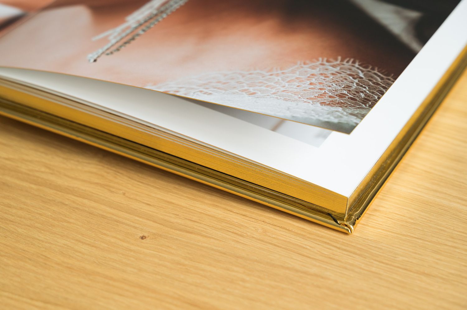 Close-up corner detail of Love Stories photo book showing gold gilded page edges on wood.