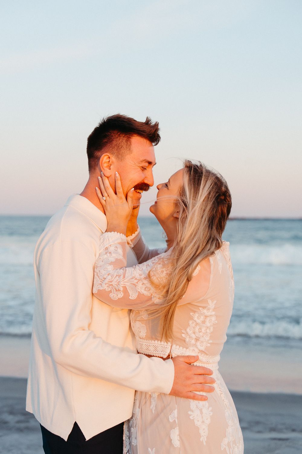 A joyful couple in wedding attire embraces and laughs together on a beach at sunset. Wedding Photographer - Wilmington NC Photographer