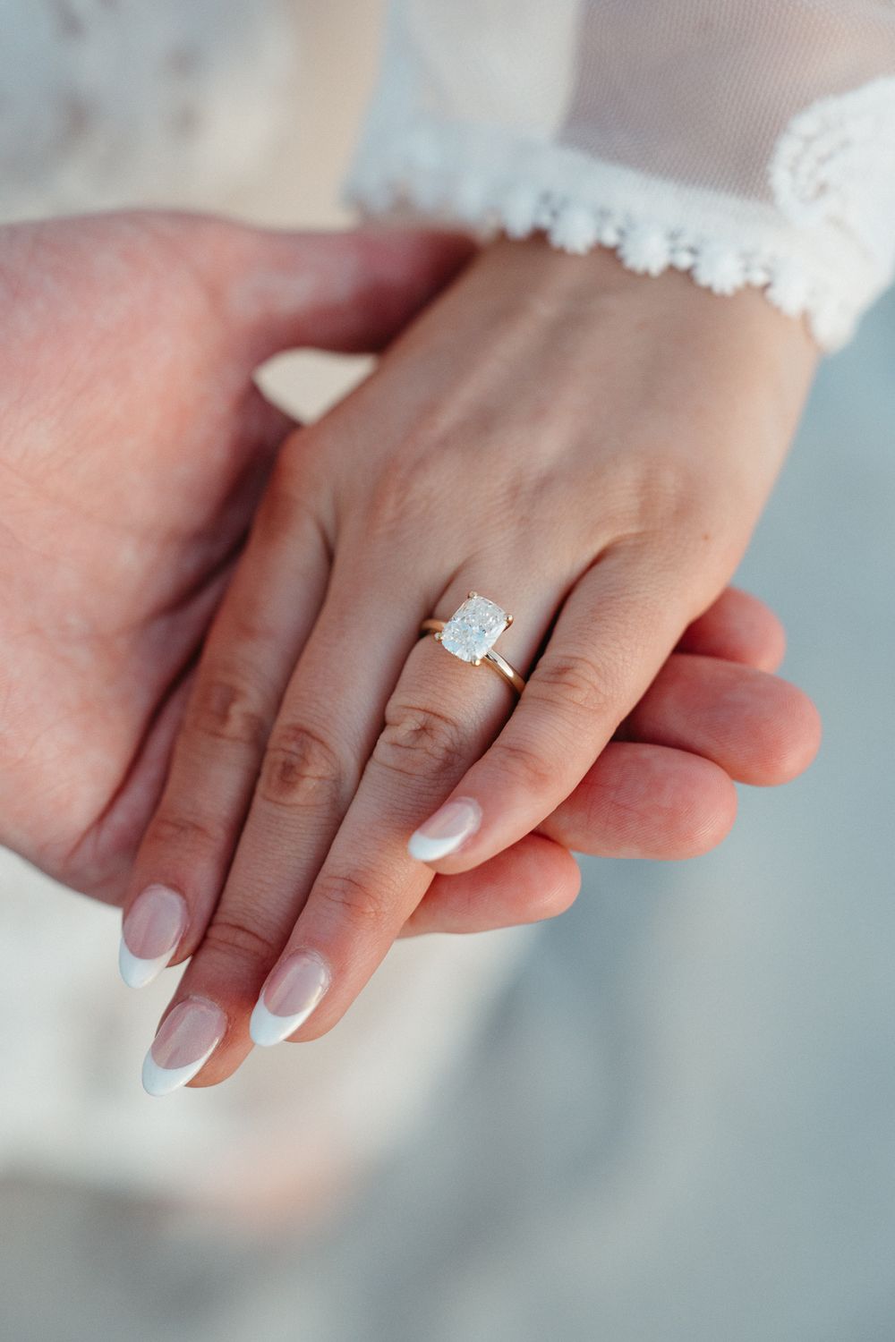 Close-up of hands showing a diamond solitaire engagement ring on gold band, with French manicure nails. Surprise Proposal at Wrightsville NC