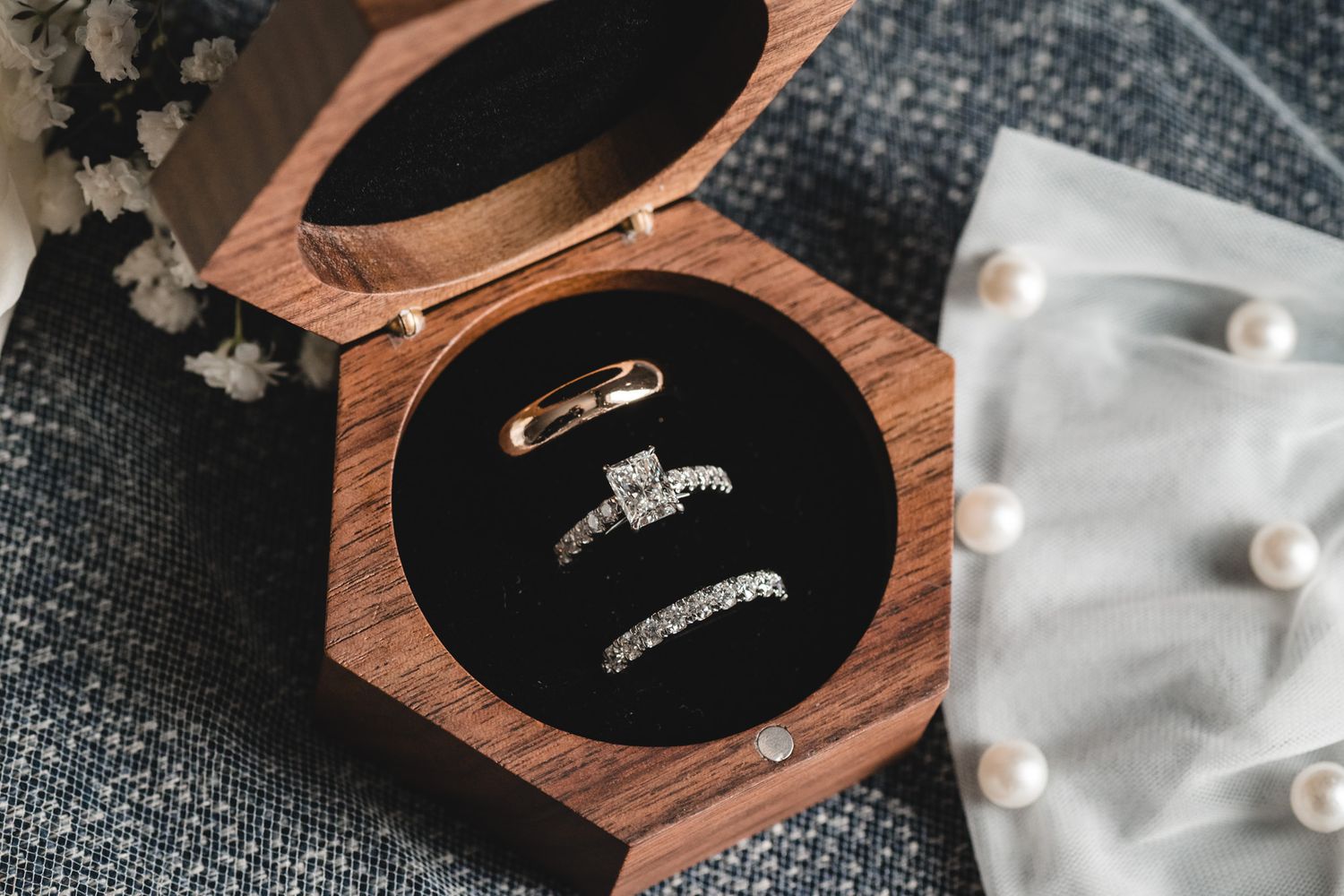 Three elegant wedding rings displayed in an open hexagonal wooden ring box lined with black velvet.