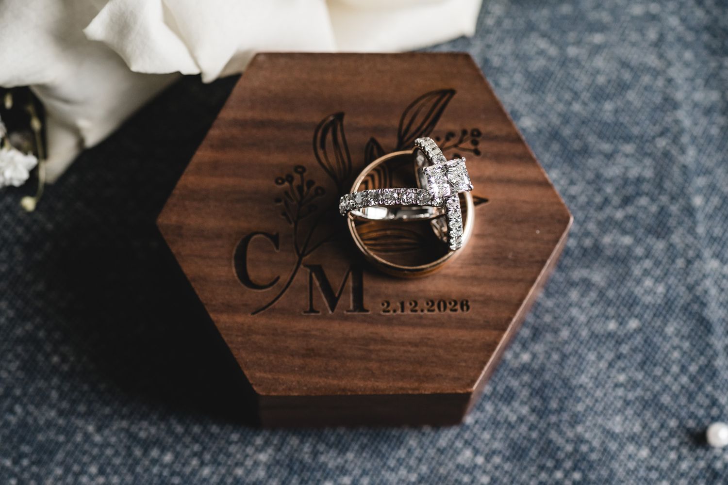 Wedding rings displayed in an engraved hexagonal wooden ring box with initials C&M and date 2.13.2026.