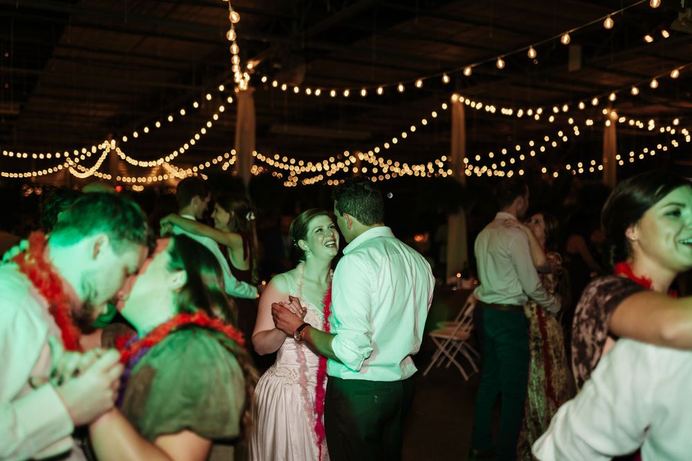 Couples dancing at a rustic wedding reception under warm string lights in a decorated barn venue.