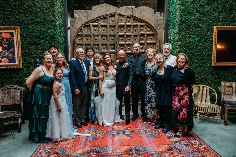 Large wedding family group photo posed in front of ivy-covered wall on colorful rug.