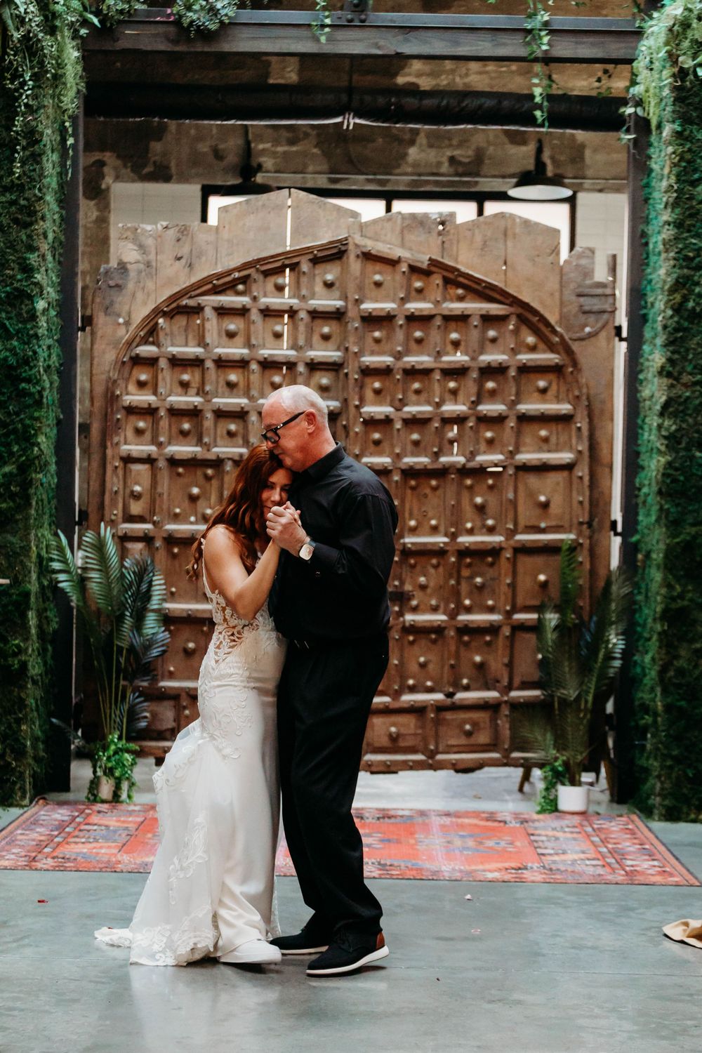 Bride and older man share a father-daughter dance before large ornate wooden doors at wedding.