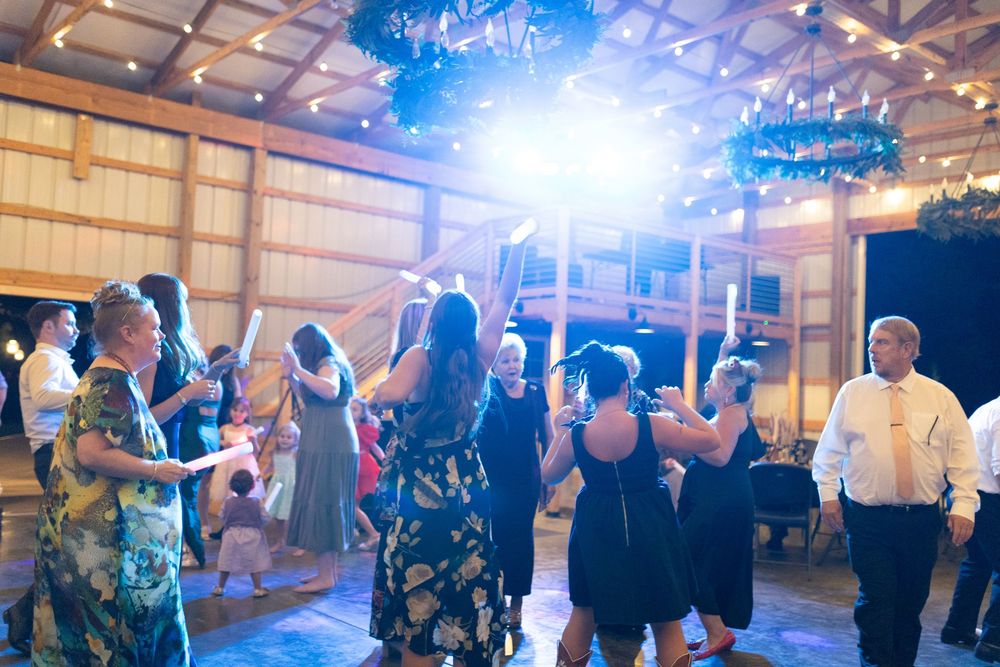 Guests dancing and celebrating with glow sticks at a rustic barn wedding reception.