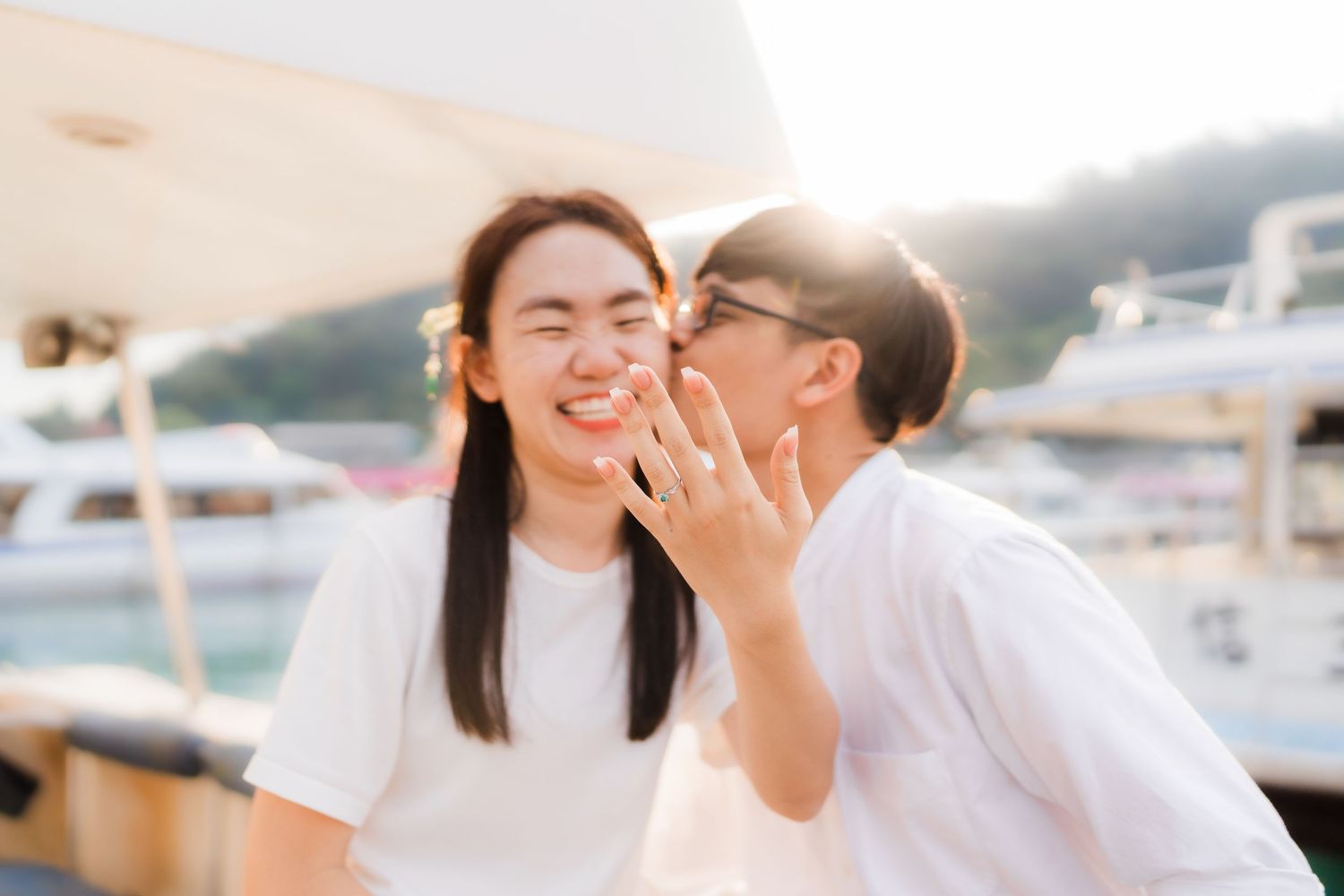 Couple sharing a romantic moment on a yacht, woman smiling as man whispers in her ear outdoors.