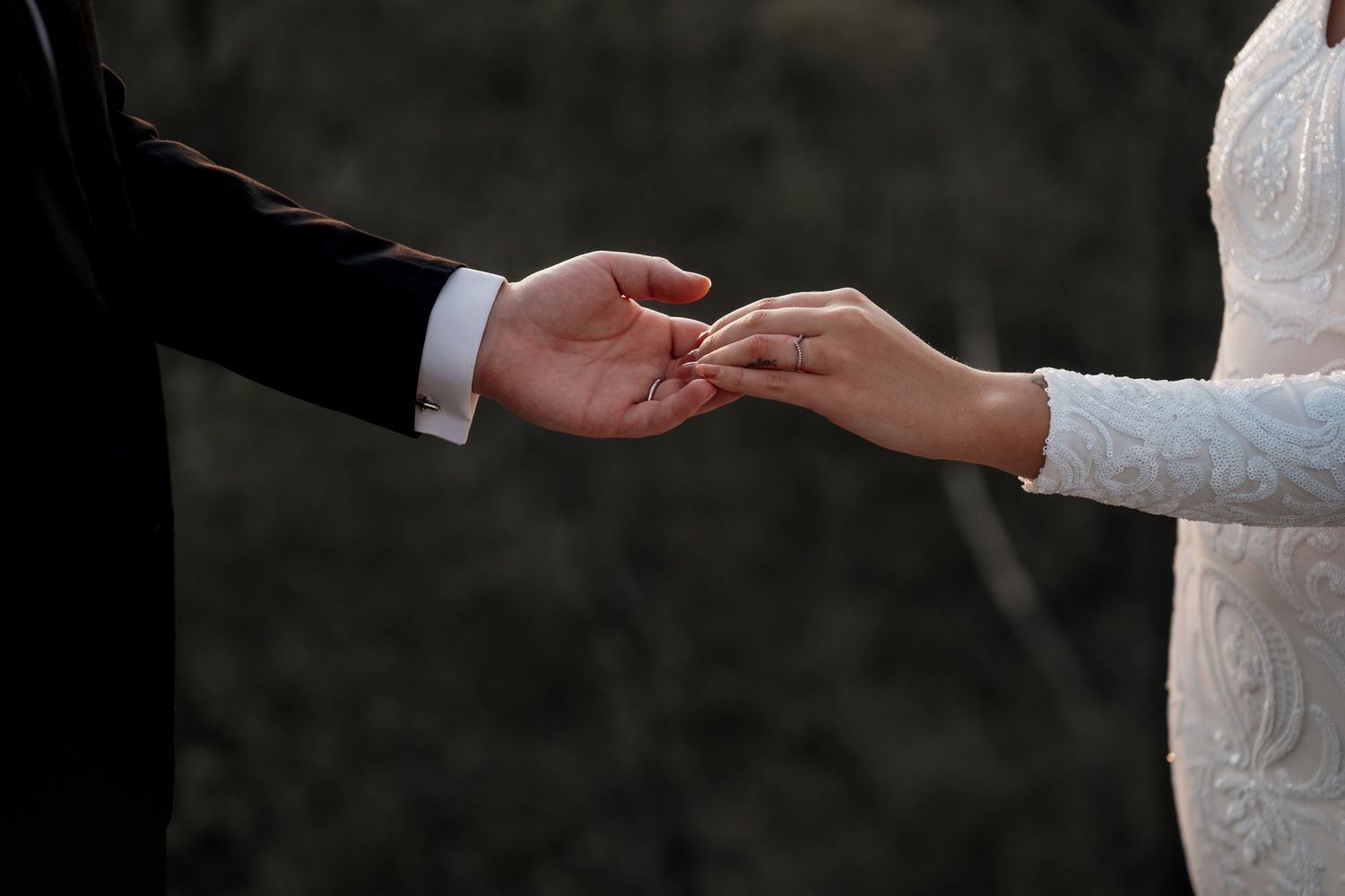 Bride and groom exchanging wedding rings during ceremony, close-up of hands in elegant wedding attire.