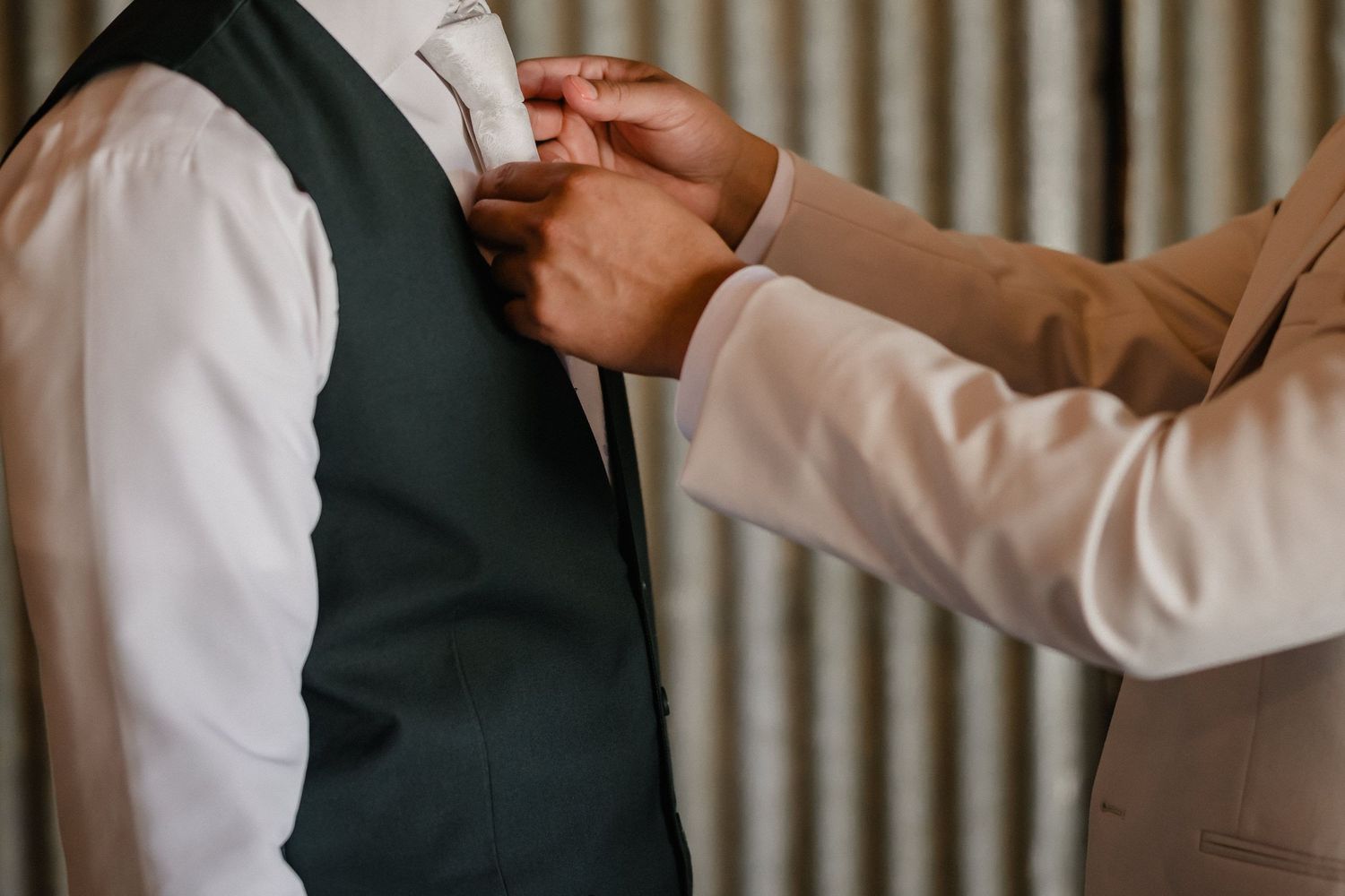 Someone adjusting a boutonniere on a groom wearing a dark green vest and tie.