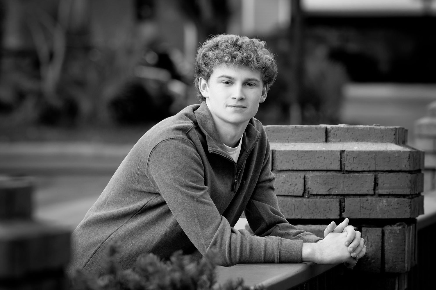 Black and white portrait of a young man leaning on a brick wall, wearing a hoodie, with a thoughtful expression.