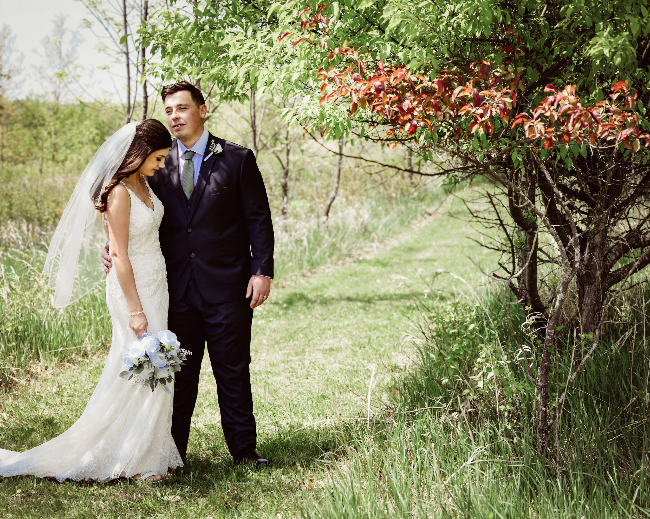Bride and groom pose together outdoors near a tree with red leaves on their wedding day.