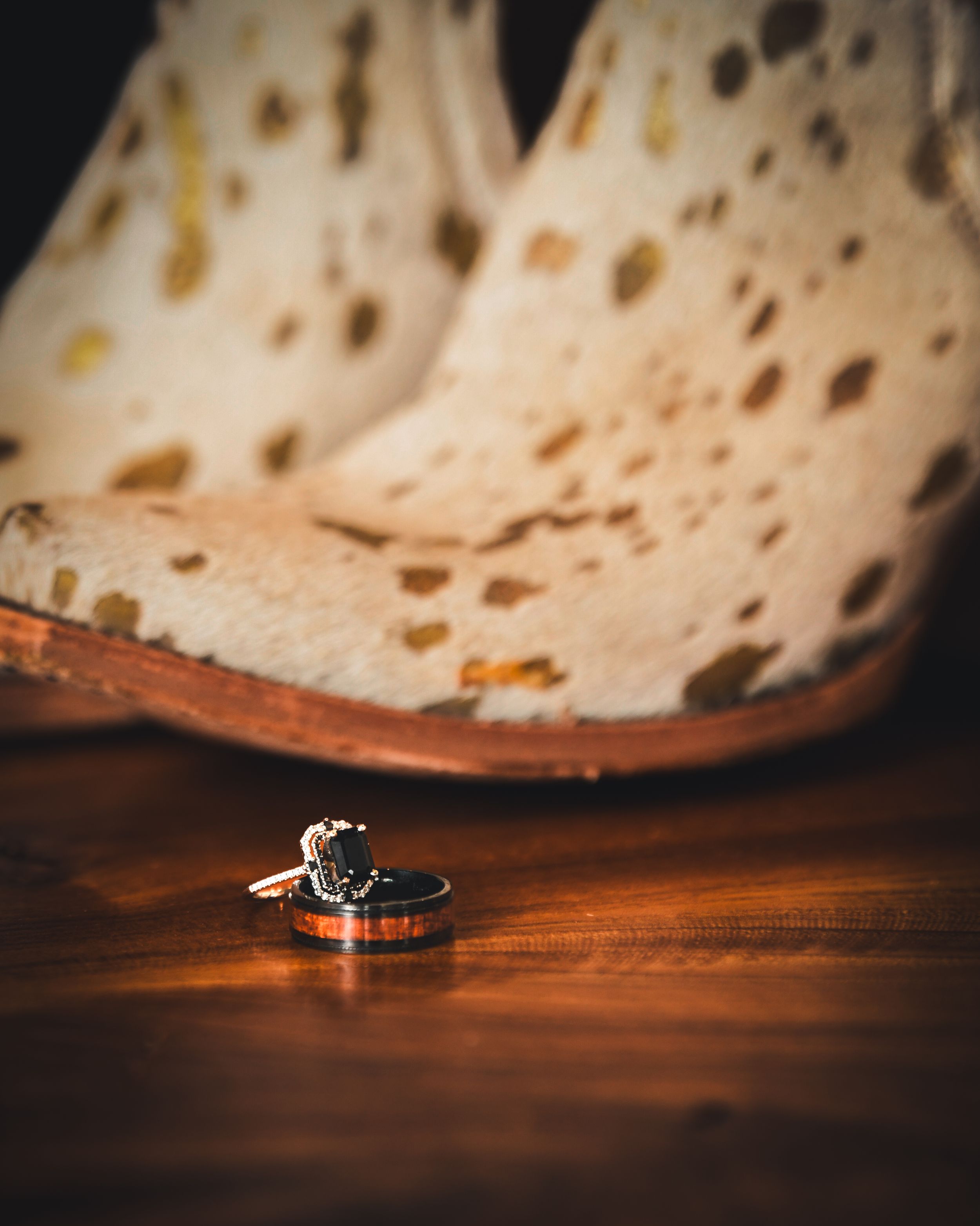 Wedding rings and engagement ring displayed on wood surface in front of cowhide western boots.
