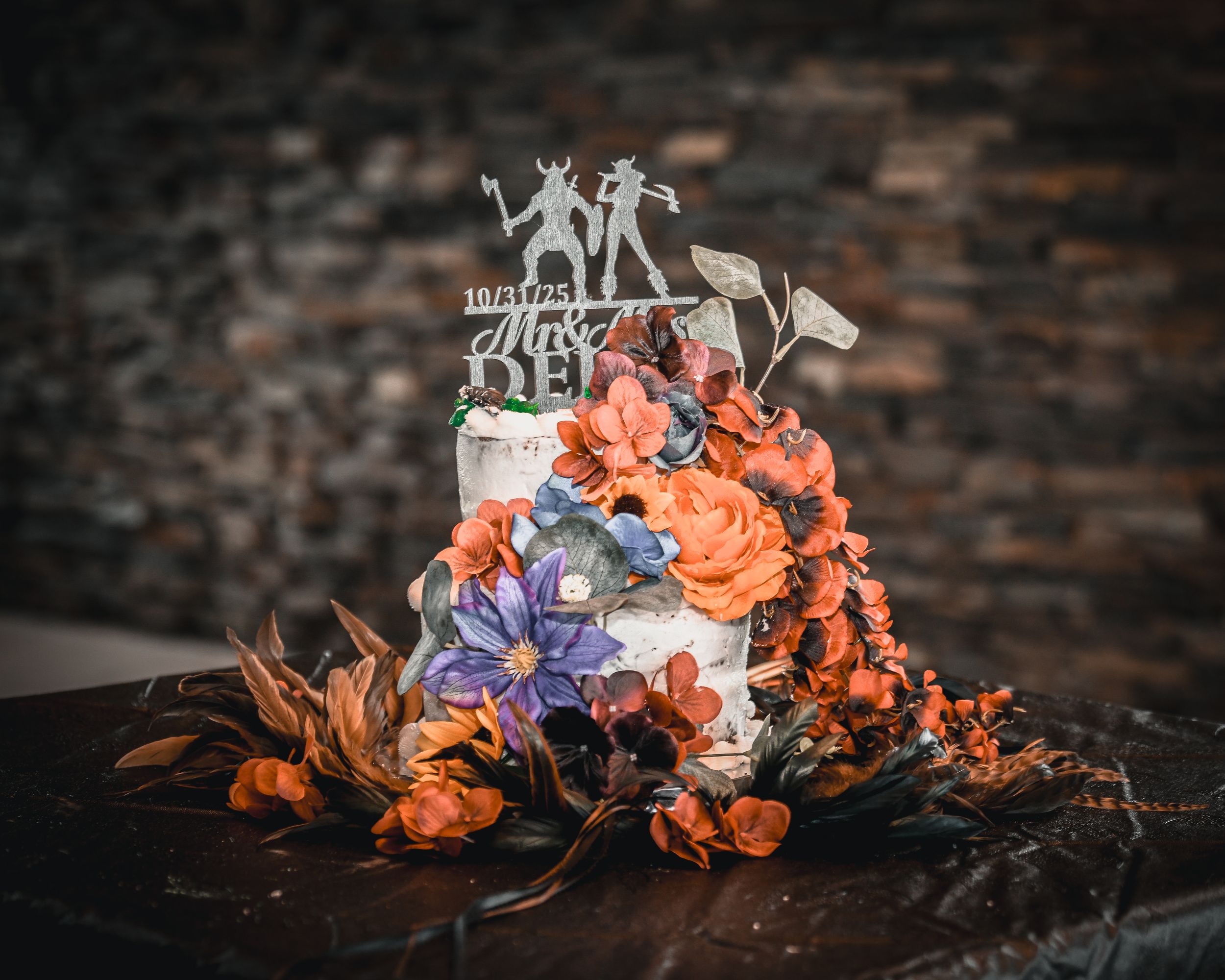 Elegant two-tier wedding cake decorated with orange and purple flowers and a silhouette cake topper.