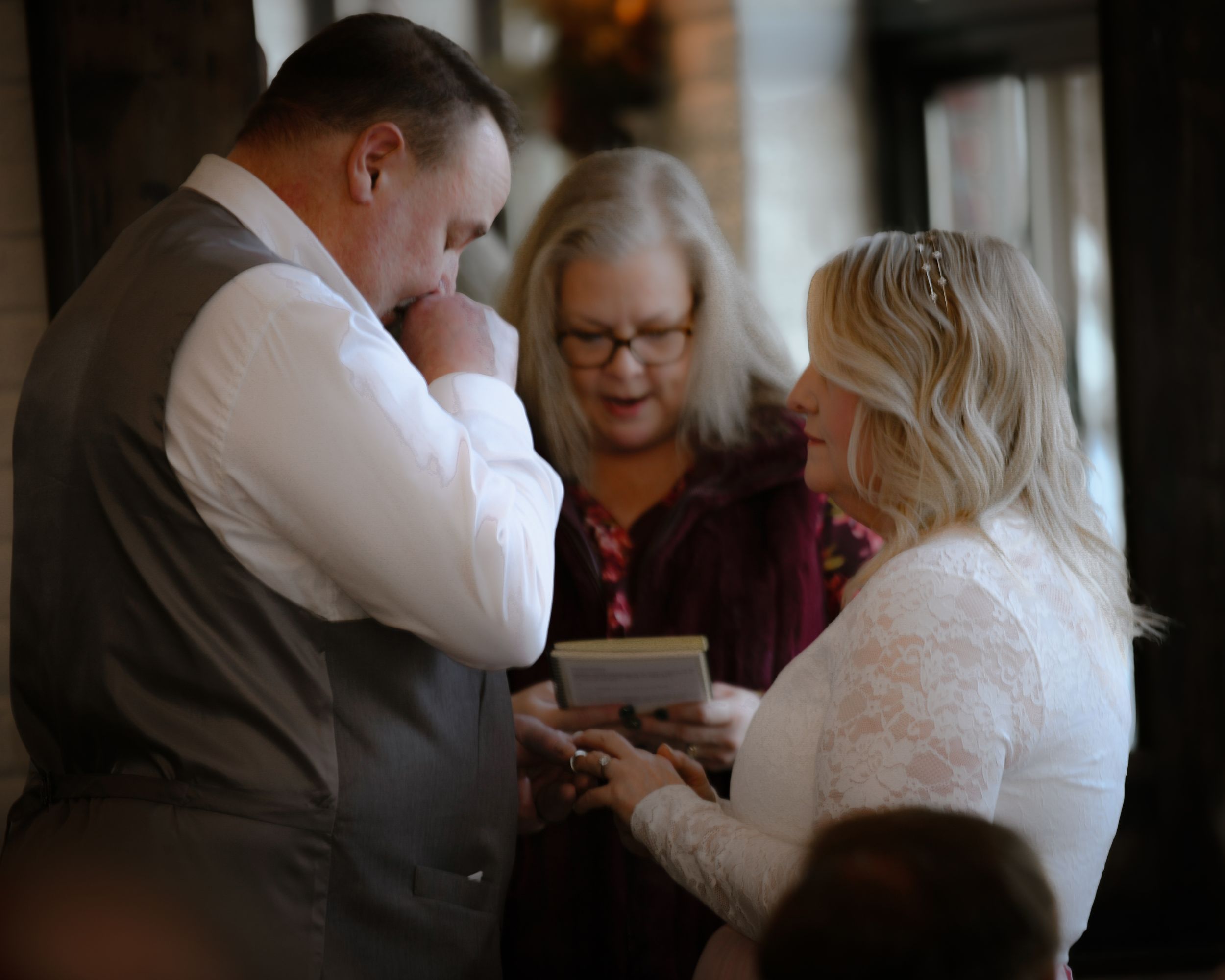 Emotional groom reading vows to bride during intimate wedding ceremony with officiant present.