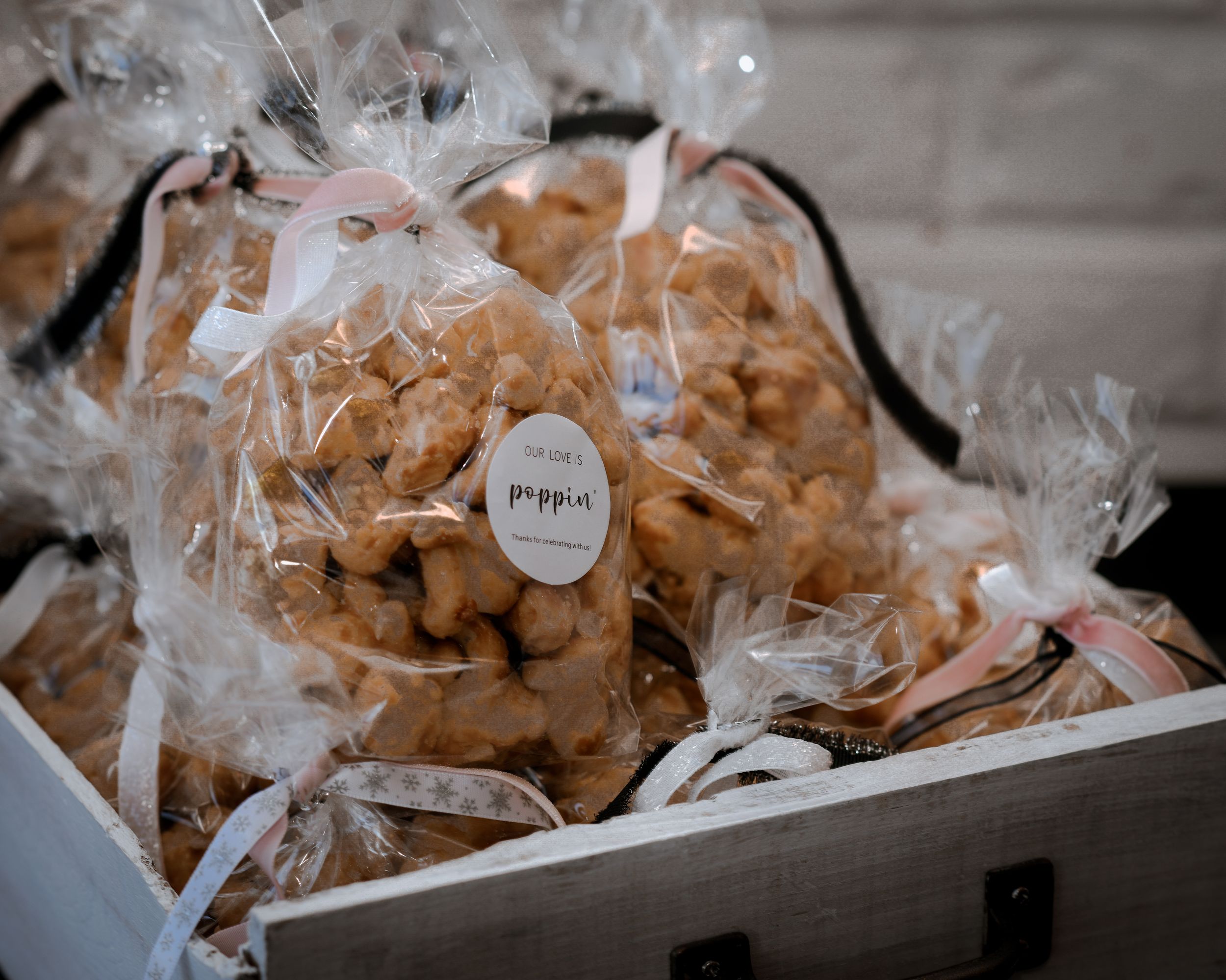 Clear bags of caramel popcorn tied with white ribbons, labeled Poppin, displayed in a wooden crate.