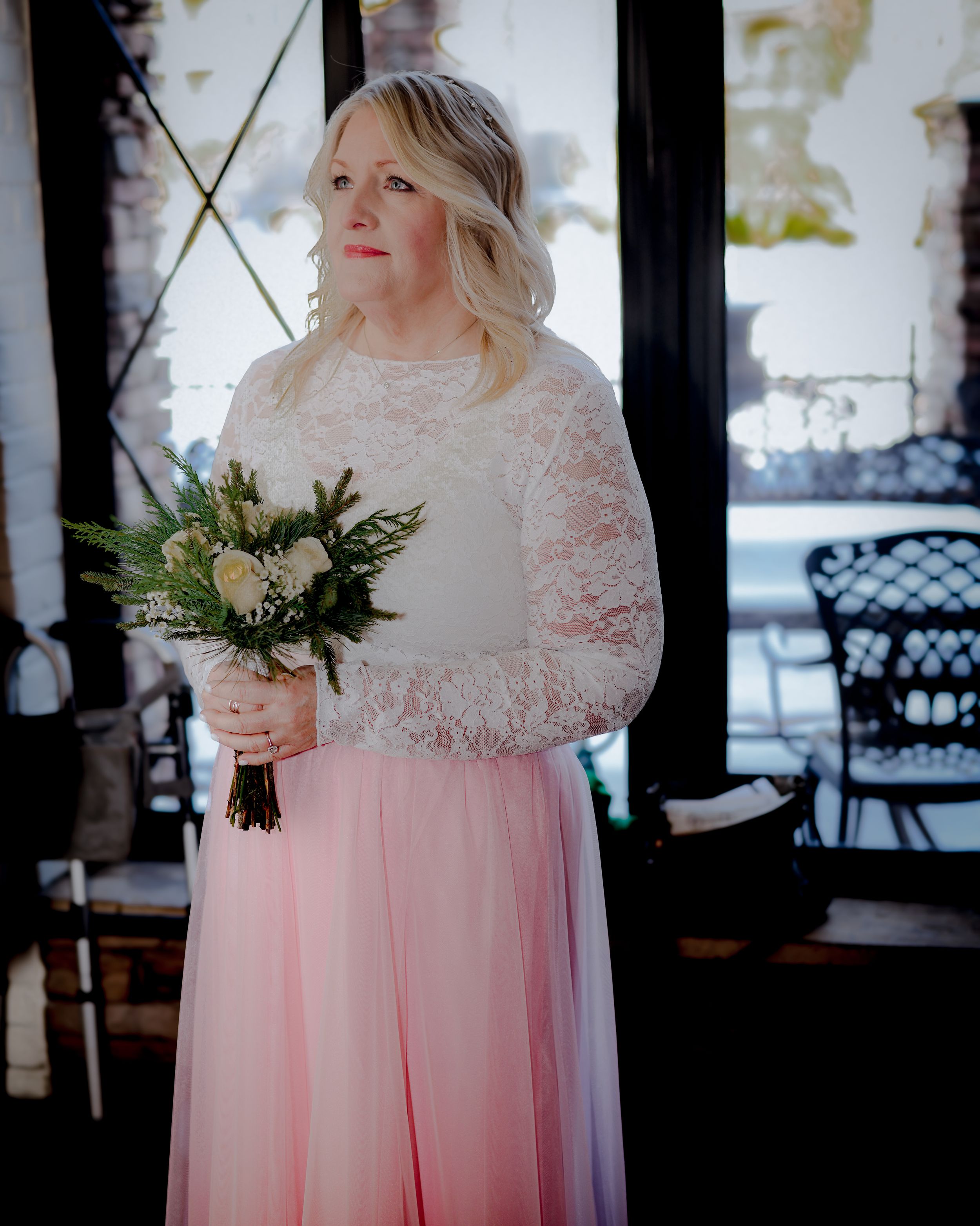 Bride in white lace top and pink tulle skirt holding a green and white bouquet at an indoor wedding venue.