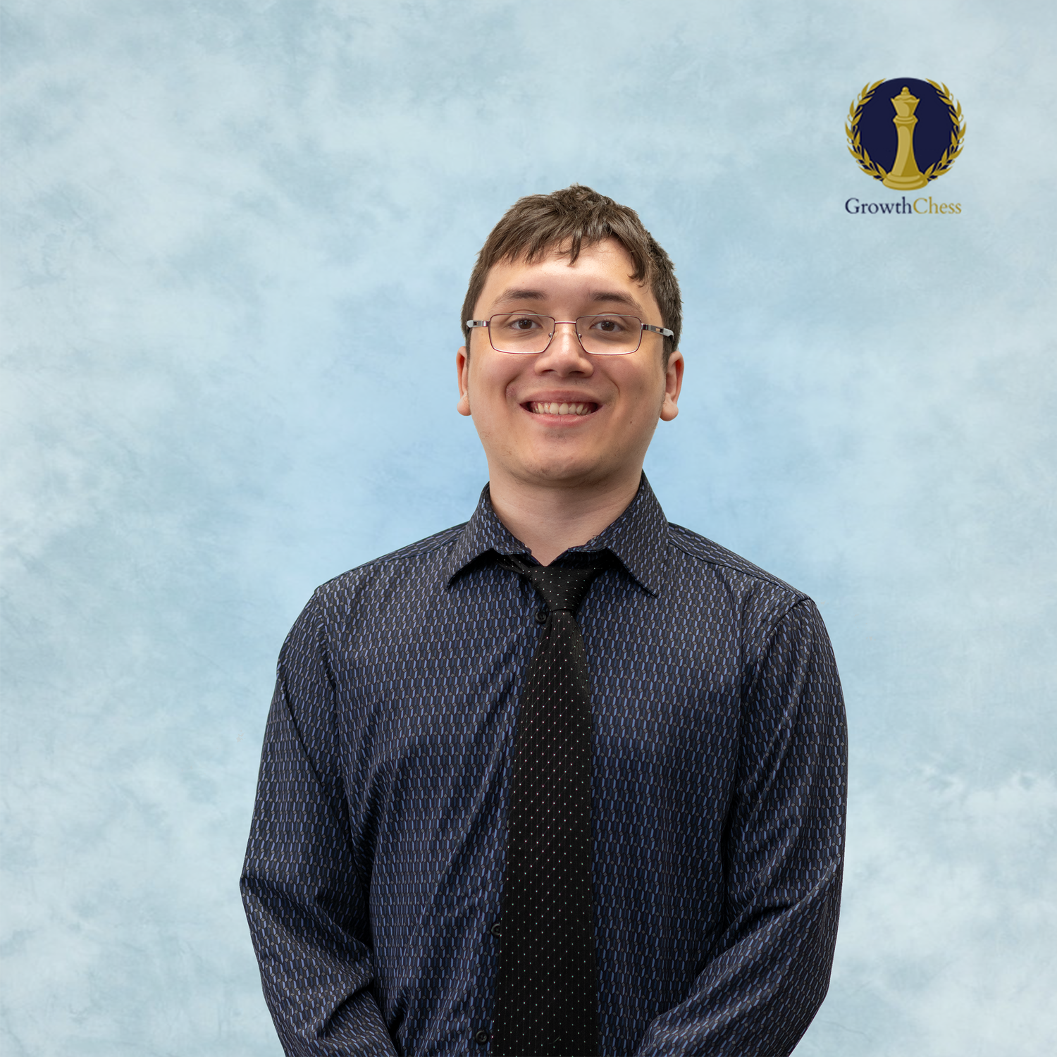Young man in dark blue patterned shirt and black tie smiling against light blue background with Growth Zone logo.