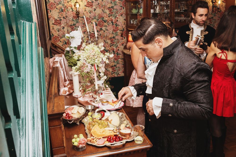 Guest serving himself food at an ornate party buffet table with floral arrangements in a vintage-style venue.