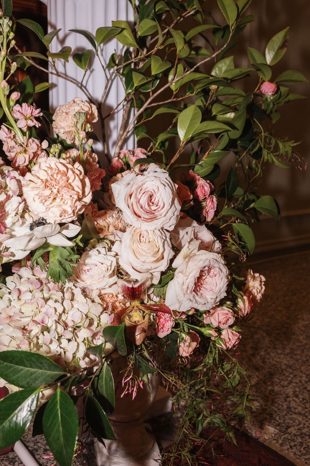 Lush floral arrangement featuring blush pink roses, peonies, hydrangeas, and green foliage in an elegant wedding centerpiece.