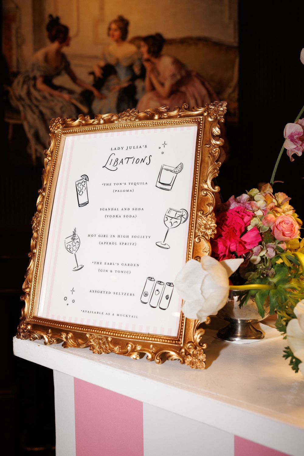 Elegant gold ornate framed cocktail menu sign displaying Lady Julia's Libations at a wedding reception with floral arrangement.
