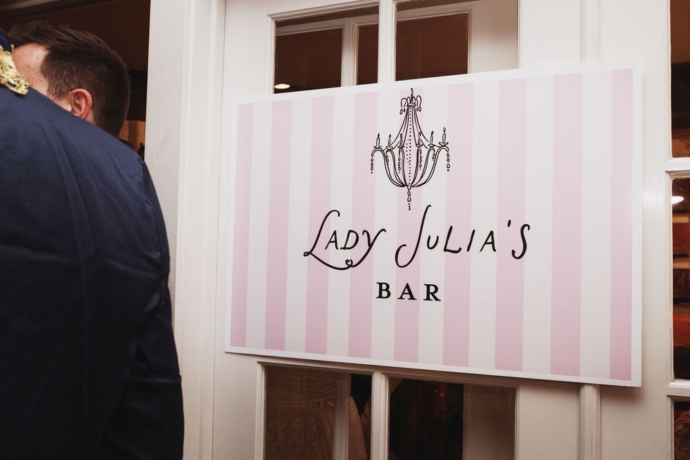Elegant pink striped sign for Lady Julia's Bar featuring a chandelier logo at an upscale event venue.