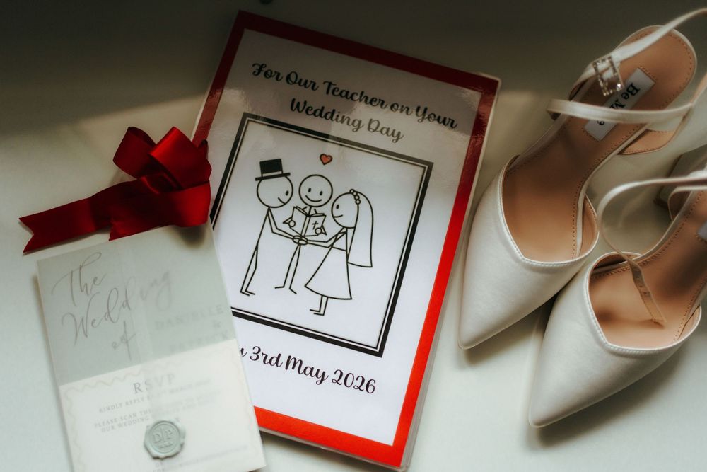 Wedding day flat lay featuring a card, white heels, red bow, and stationery dated 3rd May 2026.