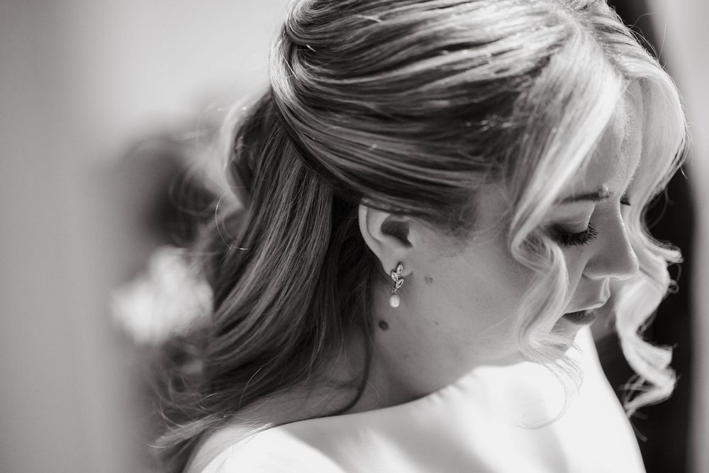Black and white portrait of a bride with elegant half-up hairstyle and pearl earring, looking down gracefully.