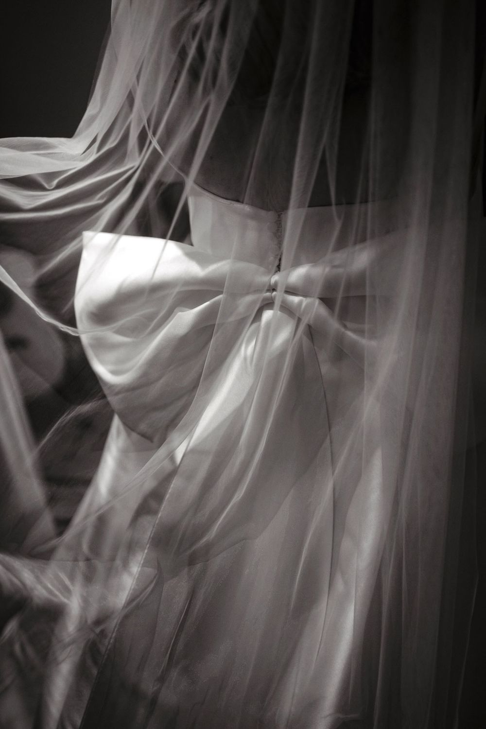 Black and white photo of an elegant wedding dress with a satin bow and flowing veil draped over a mannequin.