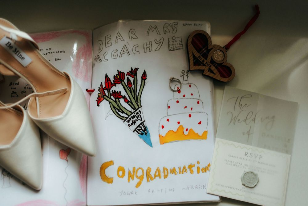 Wedding congratulations card with illustrated flowers and cake beside bridal heels and invitation.