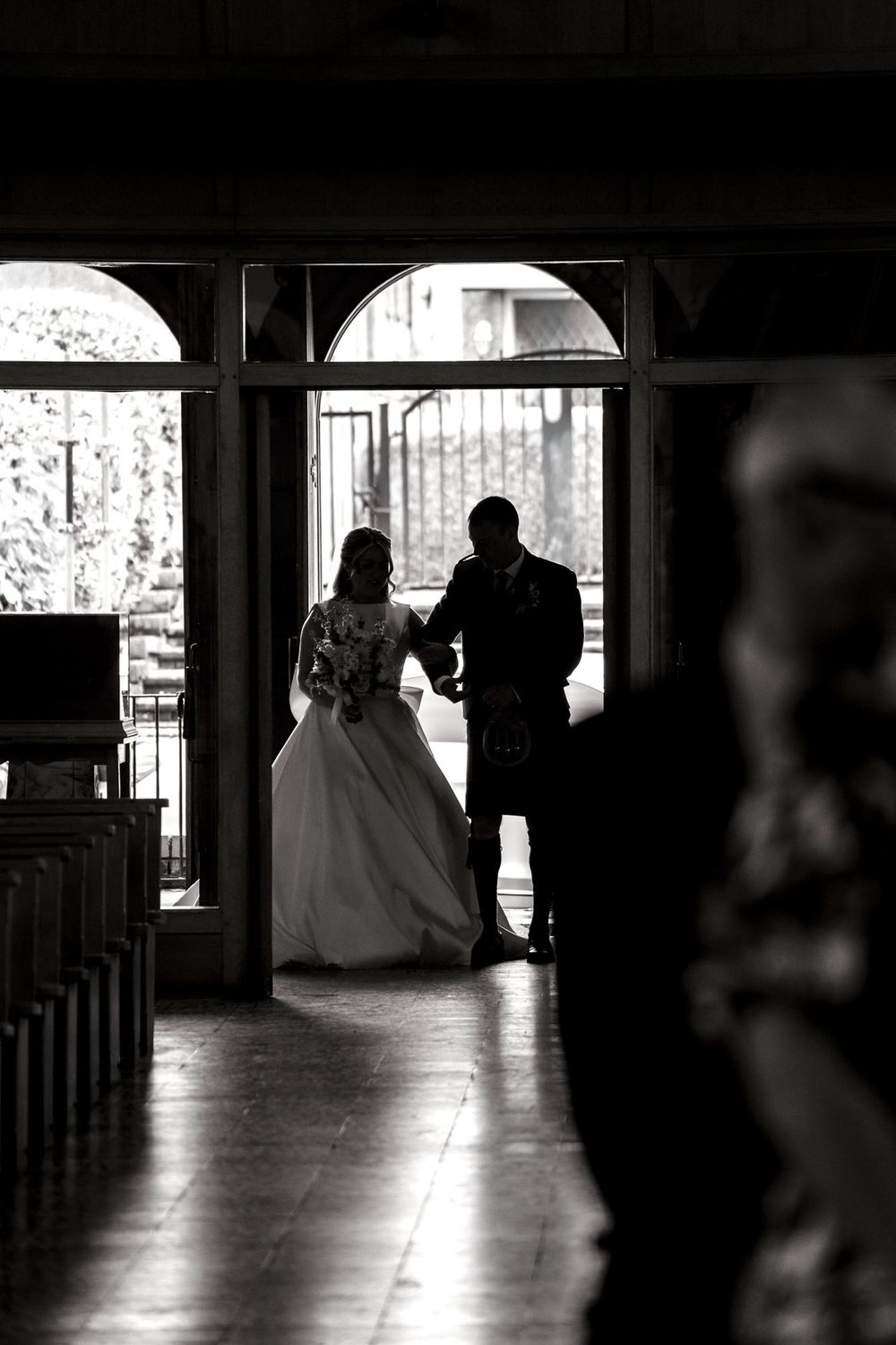 Black and white silhouette of bride and groom standing in church doorway on wedding day.