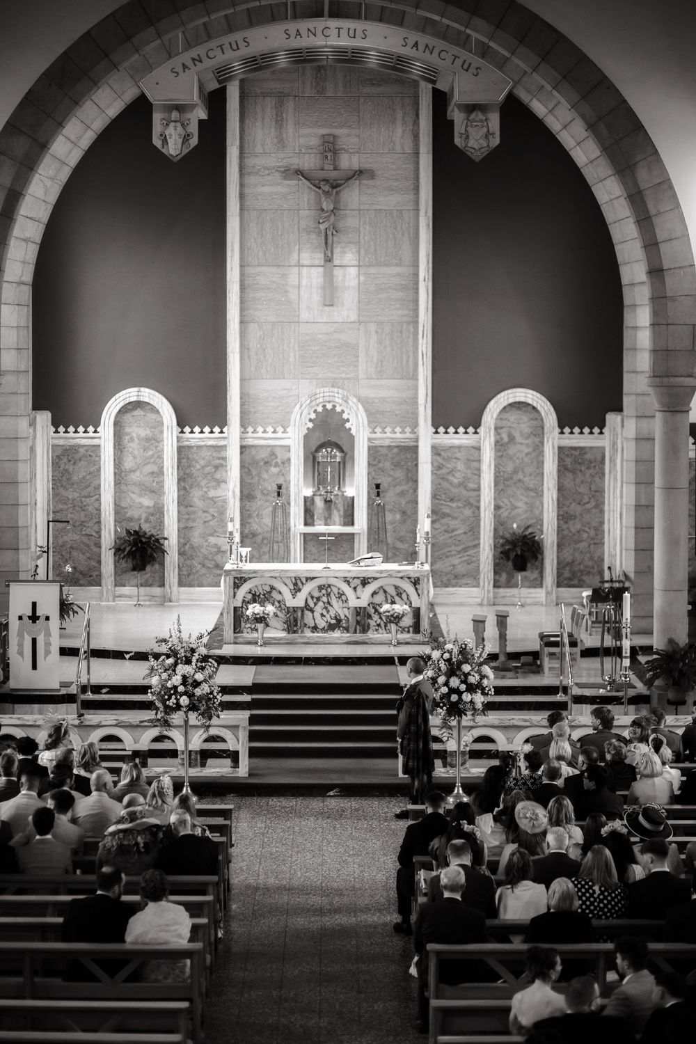 Black and white photo of a Catholic church wedding ceremony with guests seated in pews facing an ornate altar.