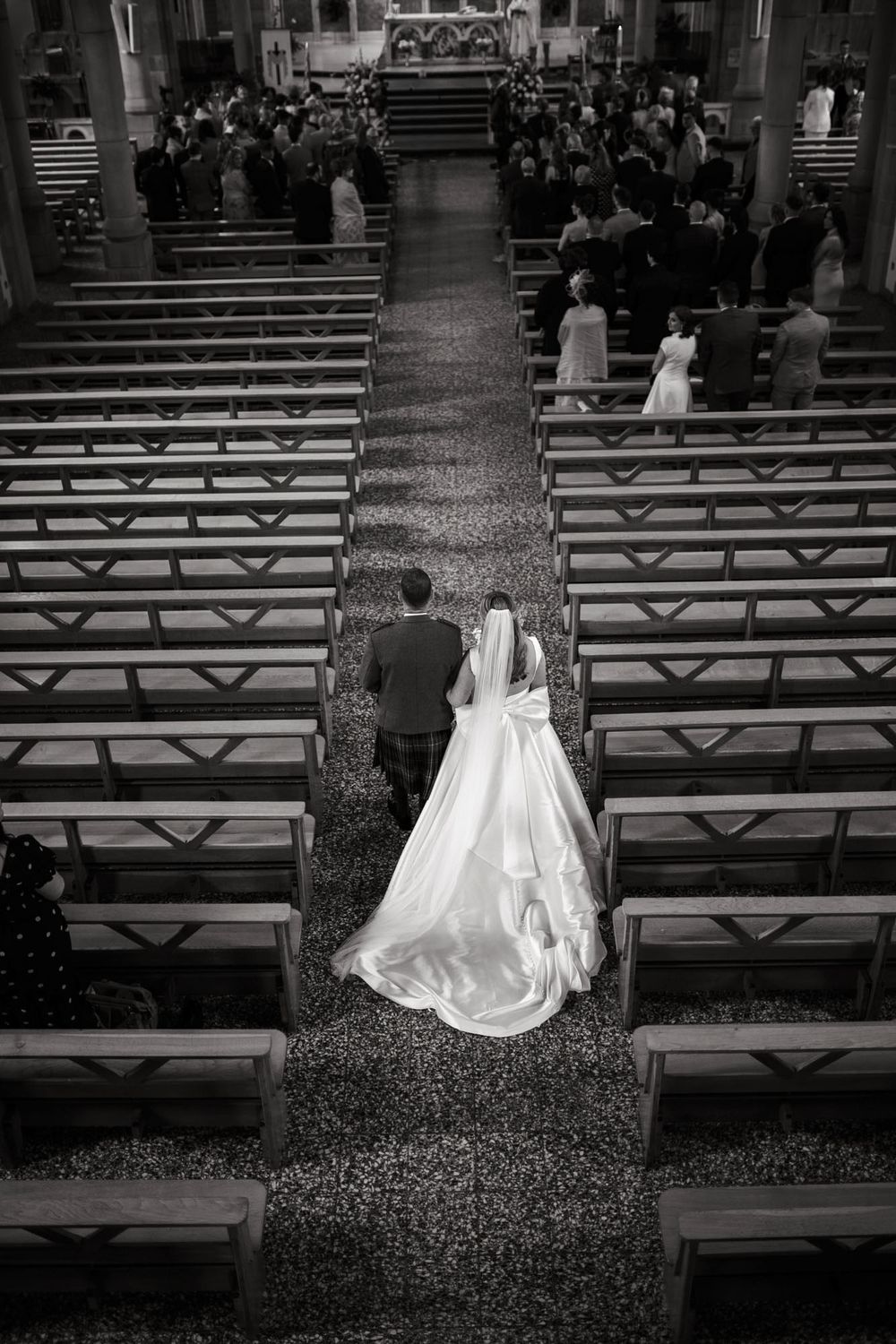 Black and white aerial view of bride and groom walking down church aisle at wedding ceremony.