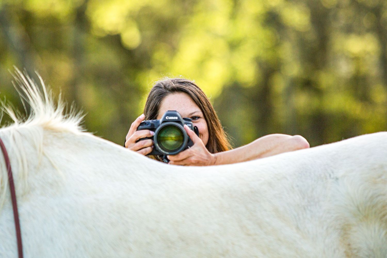 woman holding a camera looking over the back of her horse