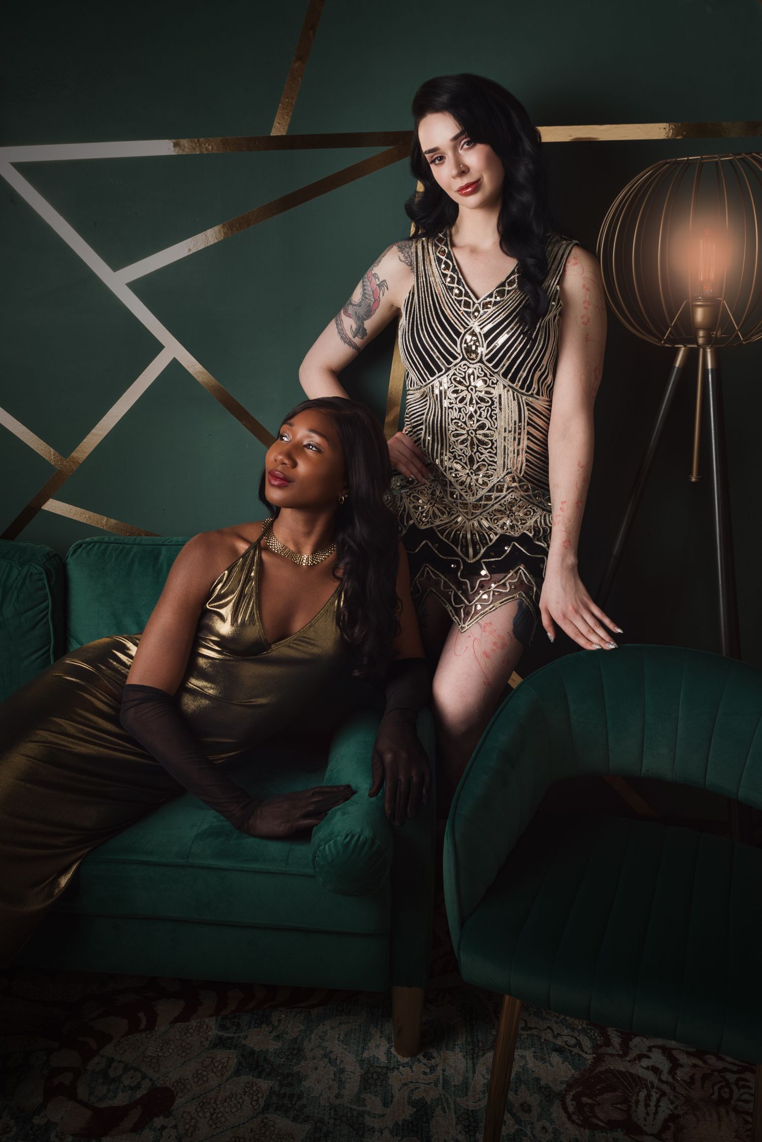 Two women in elegant gold dresses pose in a luxurious green and gold art deco styled room.