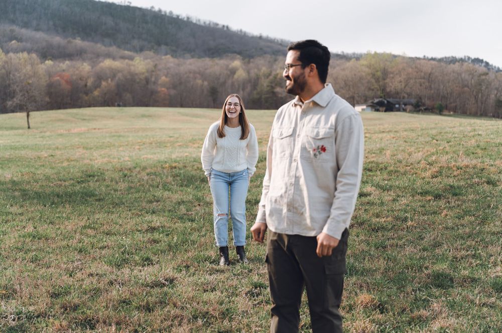 Man and woman sharing a joyful moment in an open green field with wooded hills behind them.
