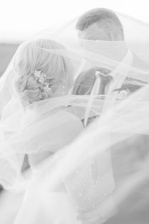 Romantic black and white photo of bride and groom embraced under flowing wedding veil.