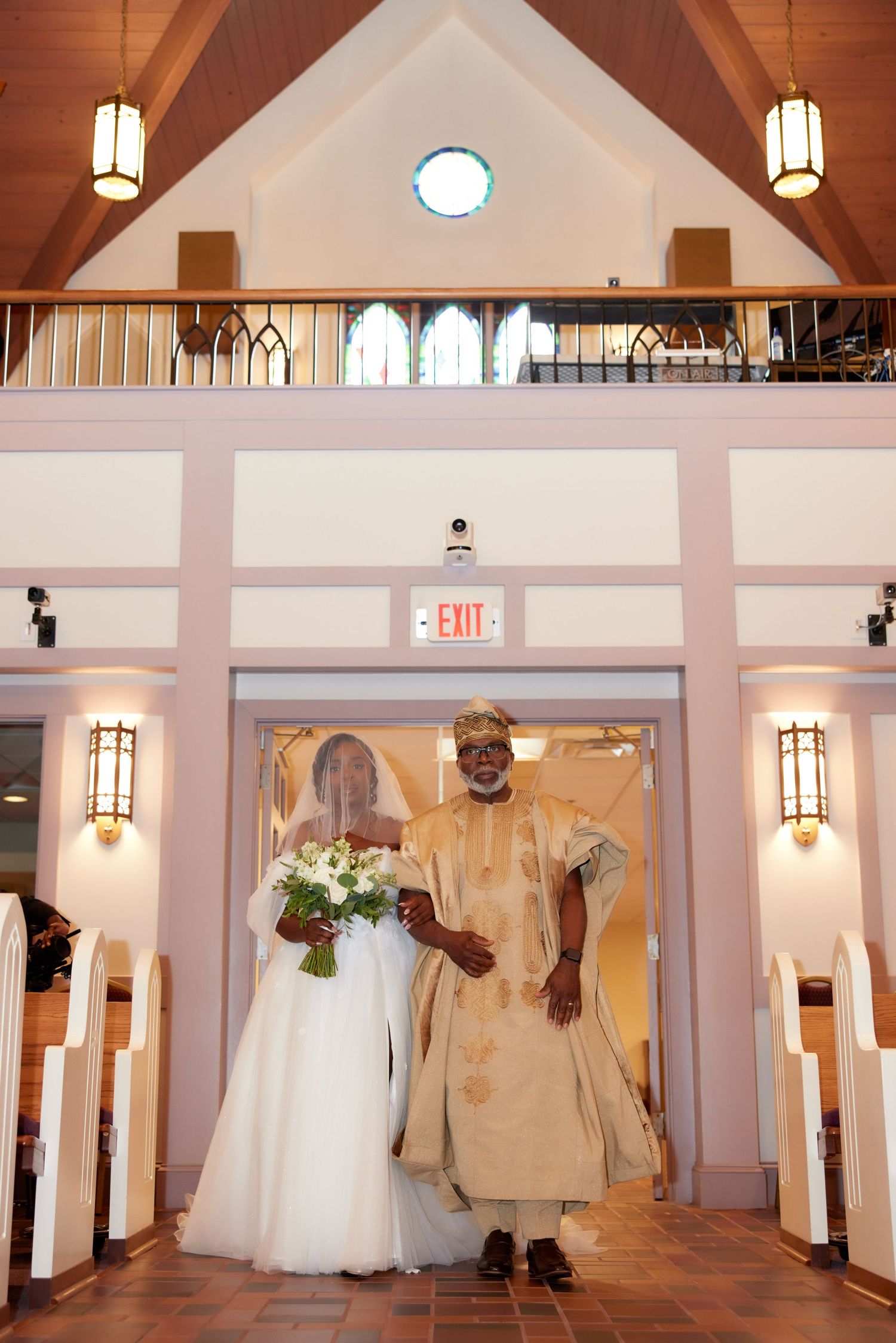 Bride in white gown and groom in gold attire walk down church aisle during wedding ceremony.